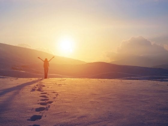 Eine Frau in bergiger Schneelandschaft schaut in die Sonne